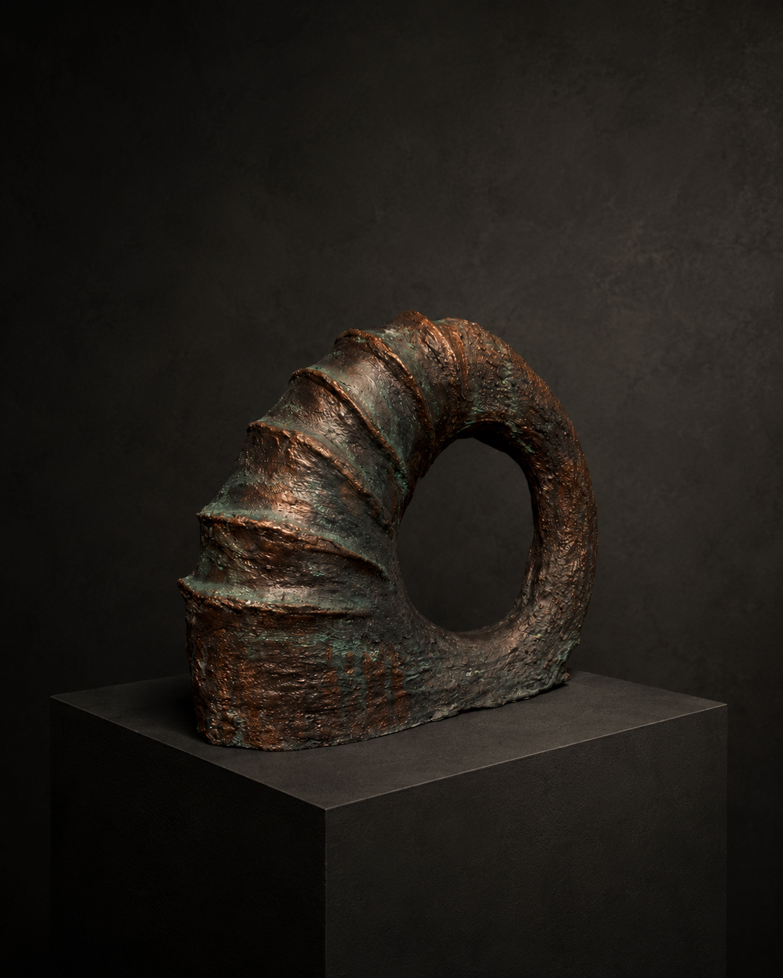 An abstract sculptural ring-like form with a textured, rusted metallic surface in brown and bronze tones, displayed on a dark pedestal against a dark studio background.